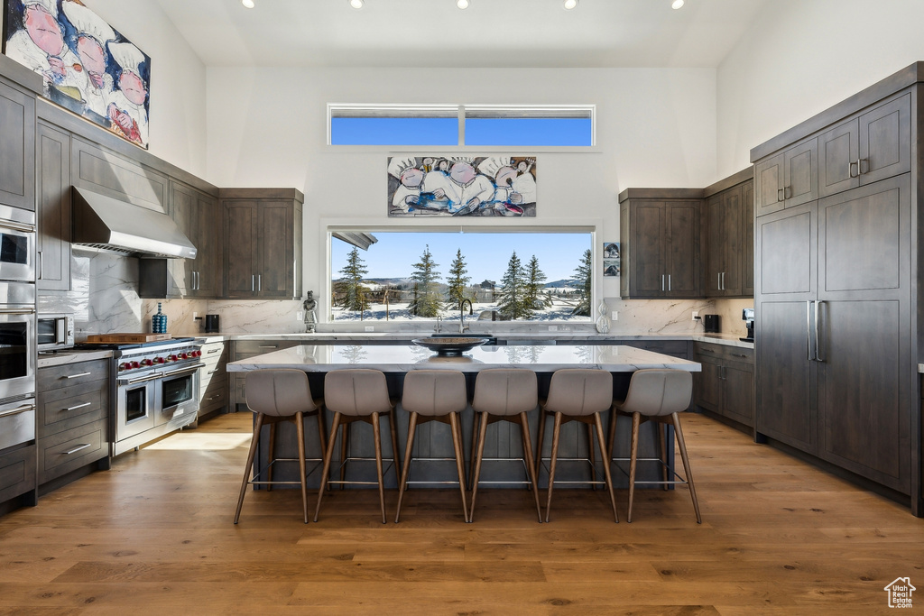 Kitchen featuring a high ceiling, decorative backsplash, recessed lighting, dark brown cabinetry, and a kitchen breakfast bar