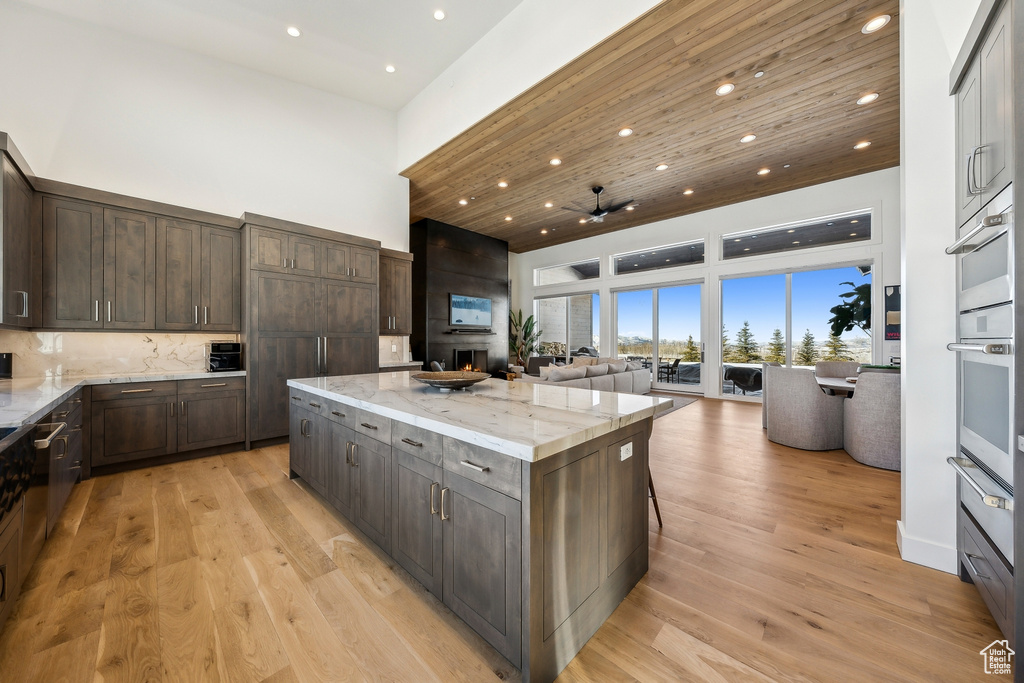 Kitchen featuring a high ceiling, open floor plan, a center island, light stone counters, and dark brown cabinets