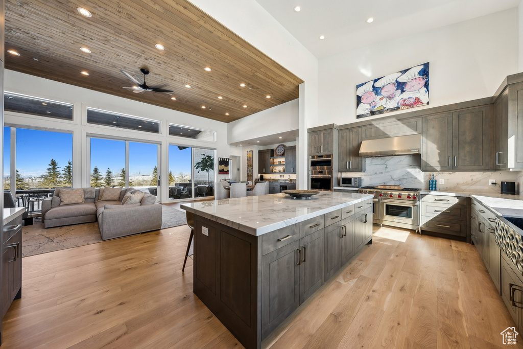 Kitchen with appliances with stainless steel finishes, a towering ceiling, wall chimney exhaust hood, a large island, and open floor plan