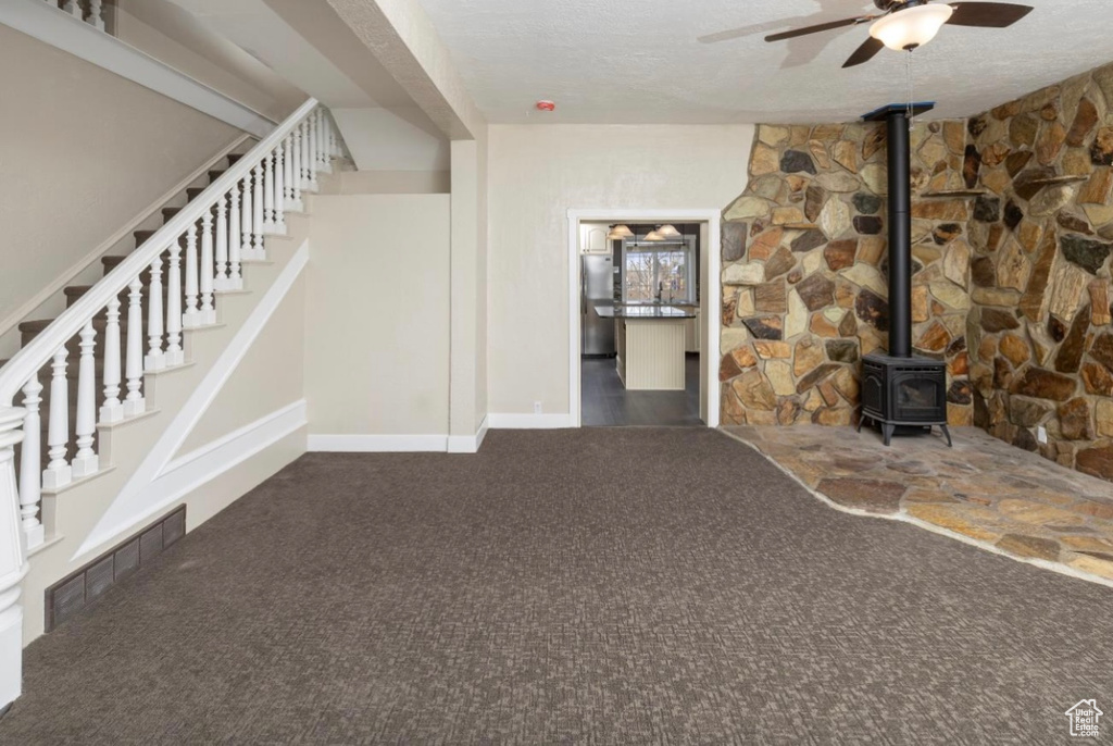 Unfurnished living room featuring visible vents, a ceiling fan, a wood stove, a textured ceiling, and carpet floors