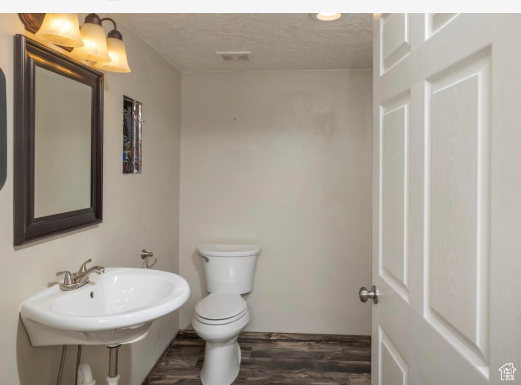 Bathroom featuring a textured ceiling, toilet, a sink, visible vents, and wood finished floors