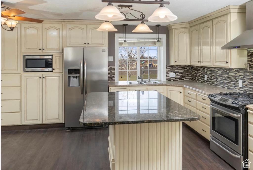 Kitchen featuring cream cabinets, stainless steel appliances, a sink, backsplash, and wall chimney exhaust hood