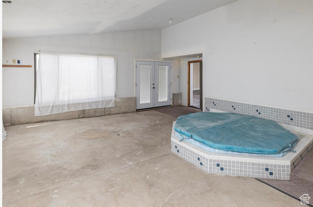 Unfurnished bedroom with vaulted ceiling, unfinished concrete flooring, and french doors