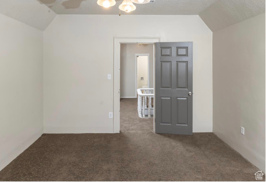 Spare room featuring carpet, vaulted ceiling, and a textured ceiling