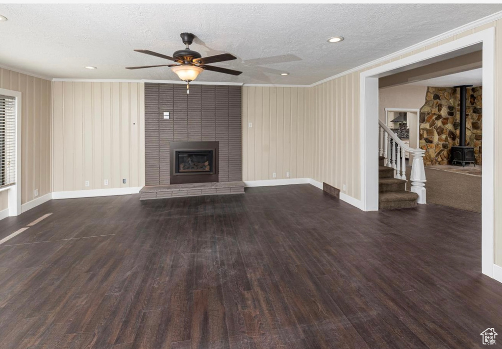 Unfurnished living room with a large fireplace, stairway, wood finished floors, and crown molding