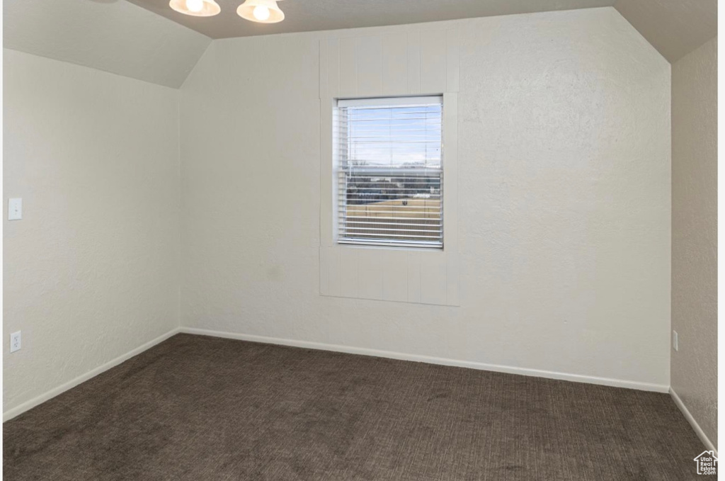 Empty room featuring vaulted ceiling, dark carpet, and baseboards