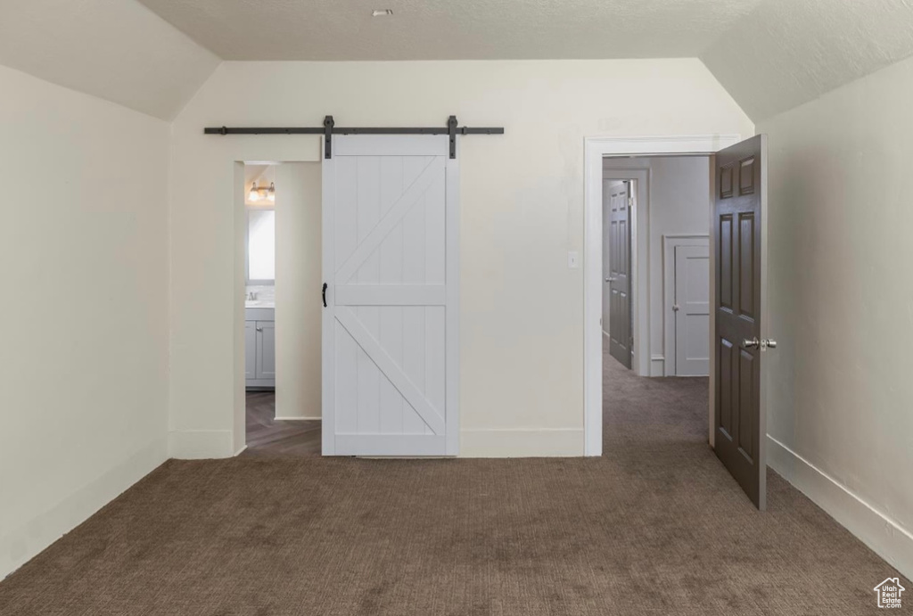 Unfurnished bedroom featuring lofted ceiling, a barn door, and carpet flooring