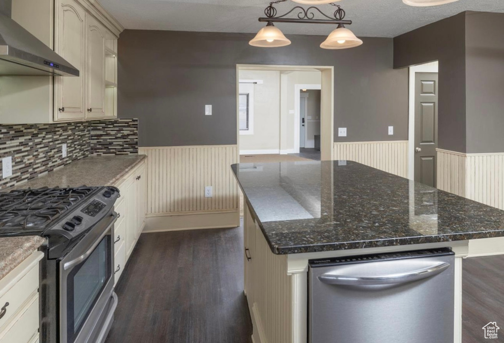 Kitchen featuring wainscoting, dark wood-style floors, dark stone countertops, wall chimney range hood, and gas stove