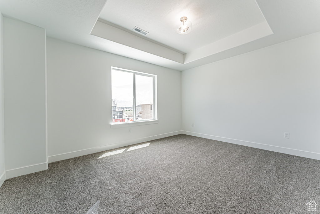 Carpeted spare room featuring a tray ceiling and baseboards
