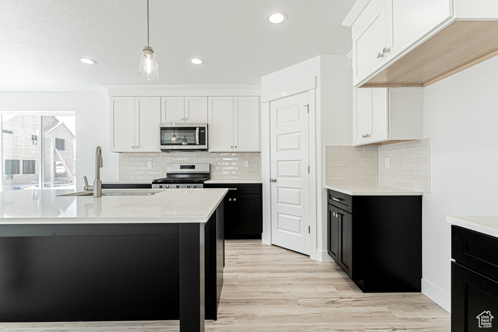 Kitchen featuring appliances with stainless steel finishes, light countertops, light wood-type flooring, recessed lighting, and decorative light fixtures