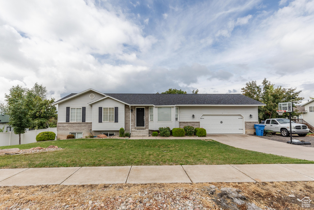 Single story home with brick siding, concrete driveway, a front yard, fence, and a garage