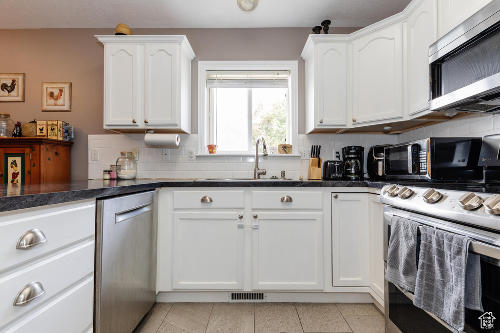 Kitchen featuring stainless steel appliances, visible vents, decorative backsplash, white cabinetry, and a sink