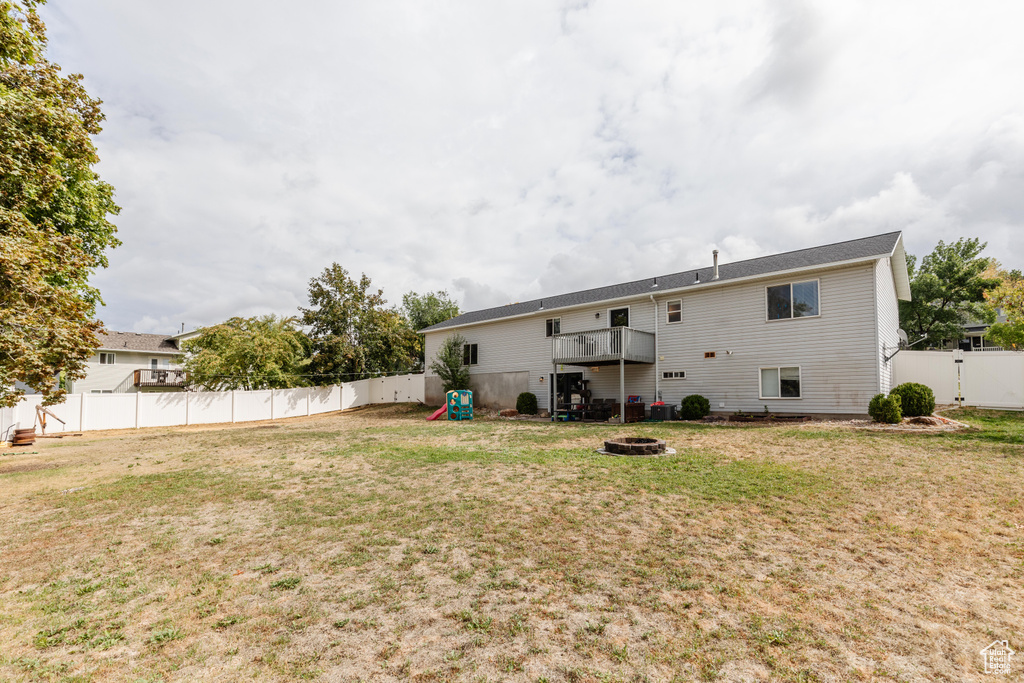 Back of property with a fenced backyard, a fire pit, and a lawn