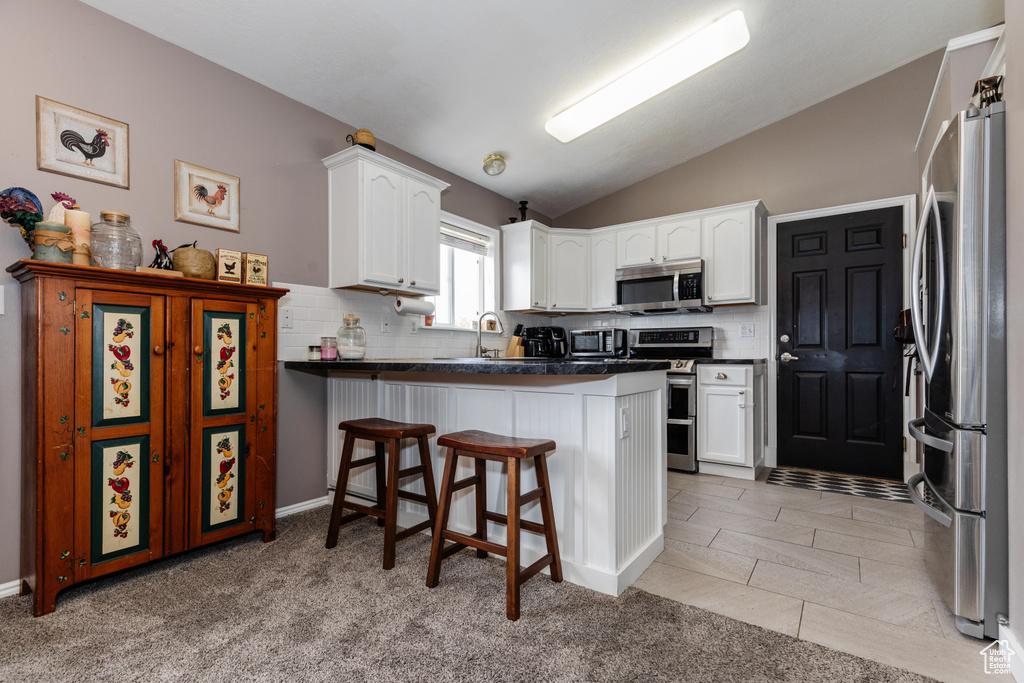 Kitchen with a peninsula, white cabinetry, vaulted ceiling, appliances with stainless steel finishes, and dark countertops