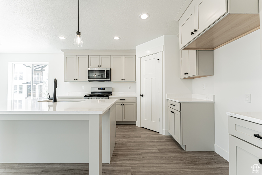 Kitchen featuring appliances with stainless steel finishes, recessed lighting, light countertops, wood finished floors, and hanging light fixtures