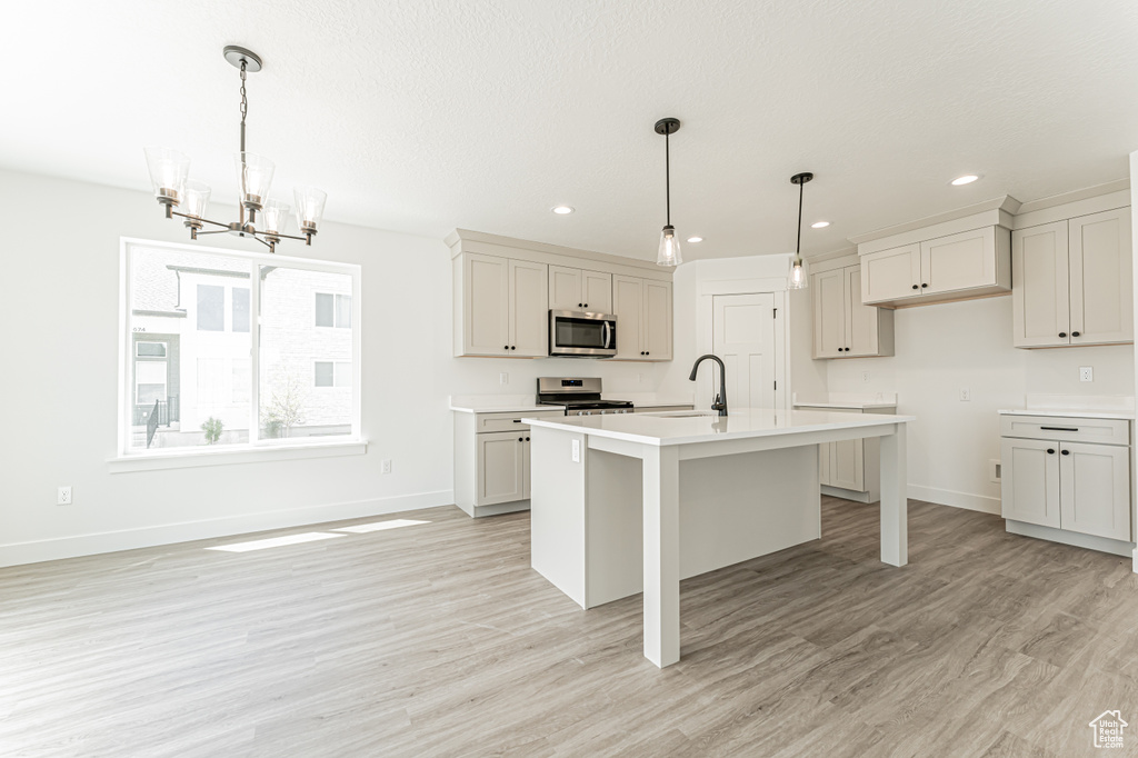 Kitchen featuring stainless steel appliances, a chandelier, a center island with sink, light countertops, and light wood-style flooring