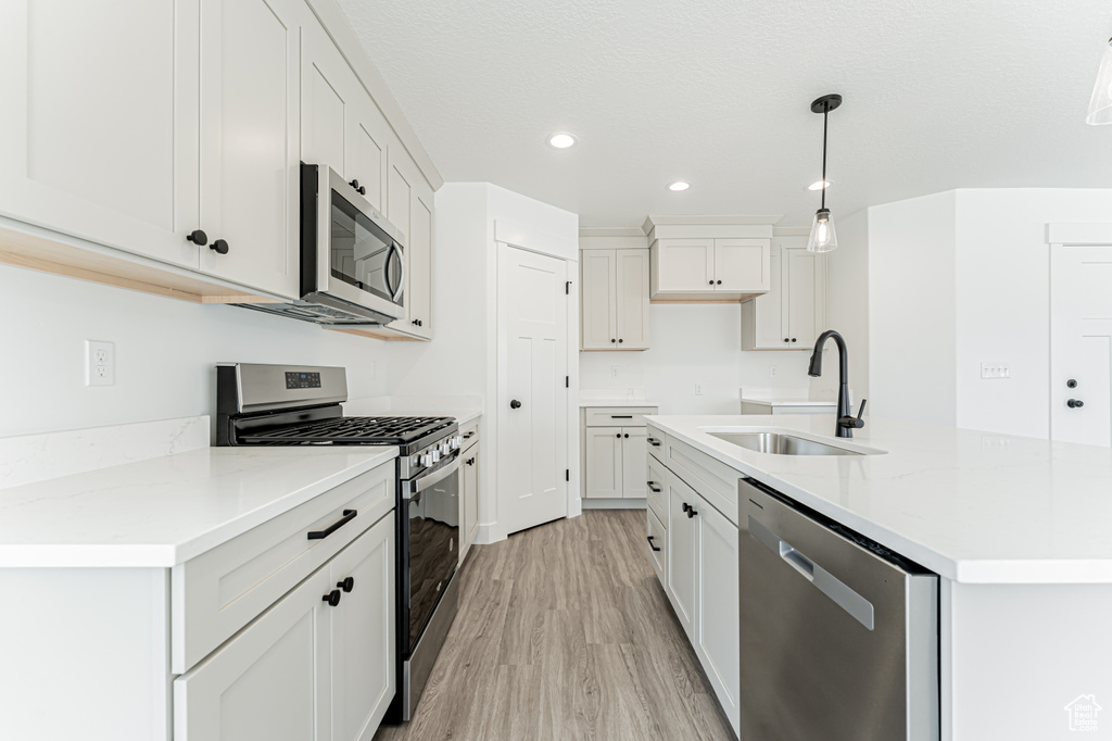 Kitchen featuring stainless steel appliances, light wood-style floors, recessed lighting, a kitchen island with sink, and hanging light fixtures