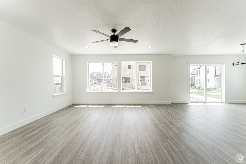 Unfurnished living room featuring ceiling fan, plenty of natural light, a chandelier, and wood finished floors