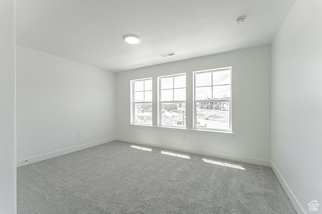 Carpeted spare room with a smoke detector and a textured ceiling