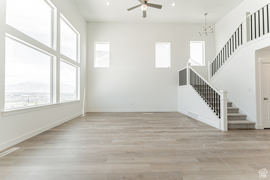 Unfurnished living room with stairs, ceiling fan, recessed lighting, light wood-style floors, and a chandelier