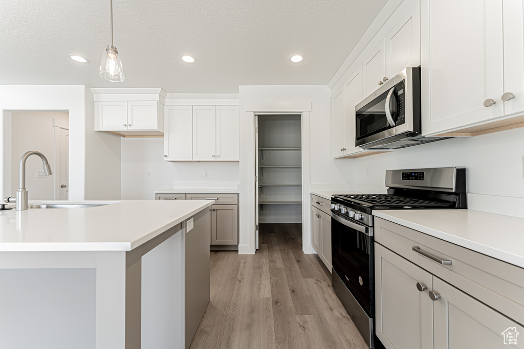 Kitchen with appliances with stainless steel finishes, light wood-style flooring, recessed lighting, light countertops, and decorative light fixtures