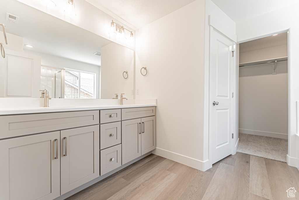 Full bathroom featuring double vanity, wood finished floors, a shower stall, and a walk in closet