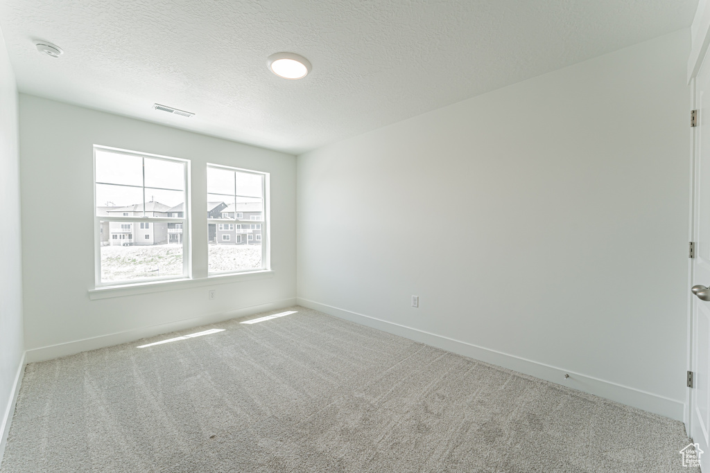Carpeted empty room featuring a textured ceiling and a smoke detector