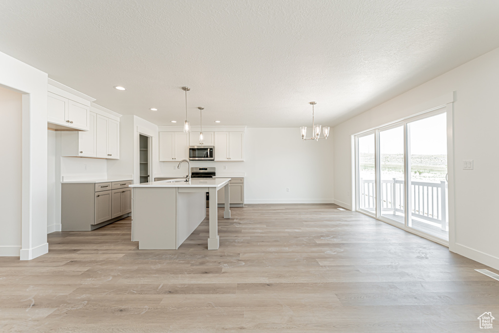 Kitchen with appliances with stainless steel finishes, a chandelier, recessed lighting, light countertops, and a center island with sink