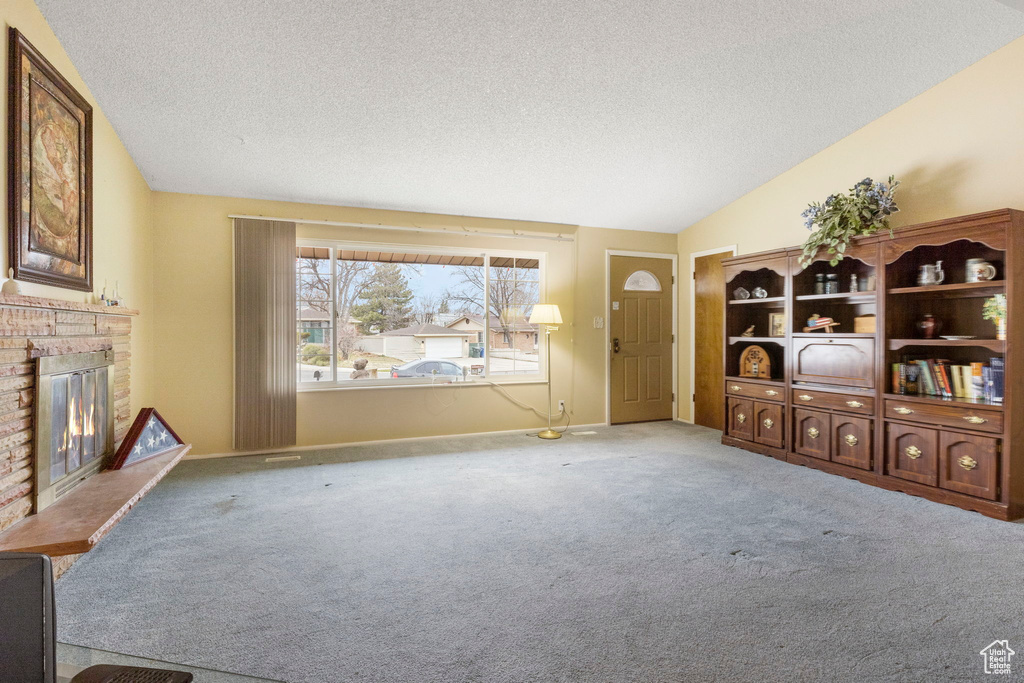 Living area featuring lofted ceiling, a brick fireplace, a textured ceiling, and carpet flooring