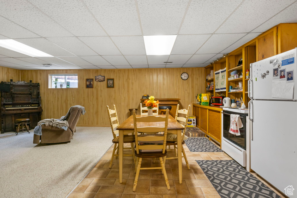 Dining area featuring a paneled ceiling, wood walls, and light colored carpet