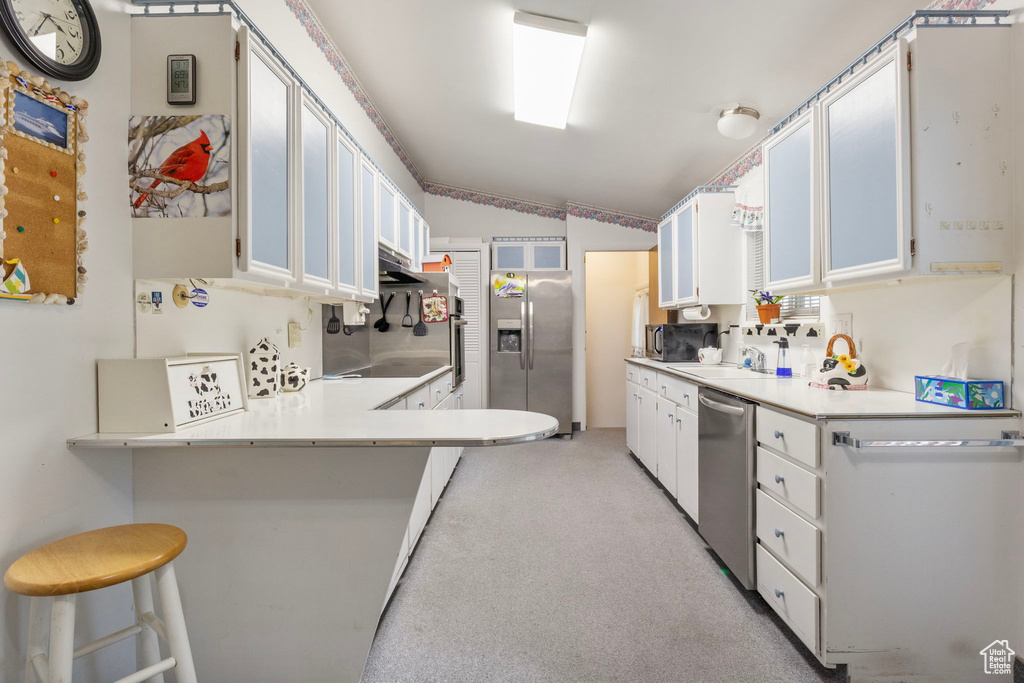 Kitchen featuring lofted ceiling, a breakfast bar area, stainless steel appliances, a peninsula, and light countertops