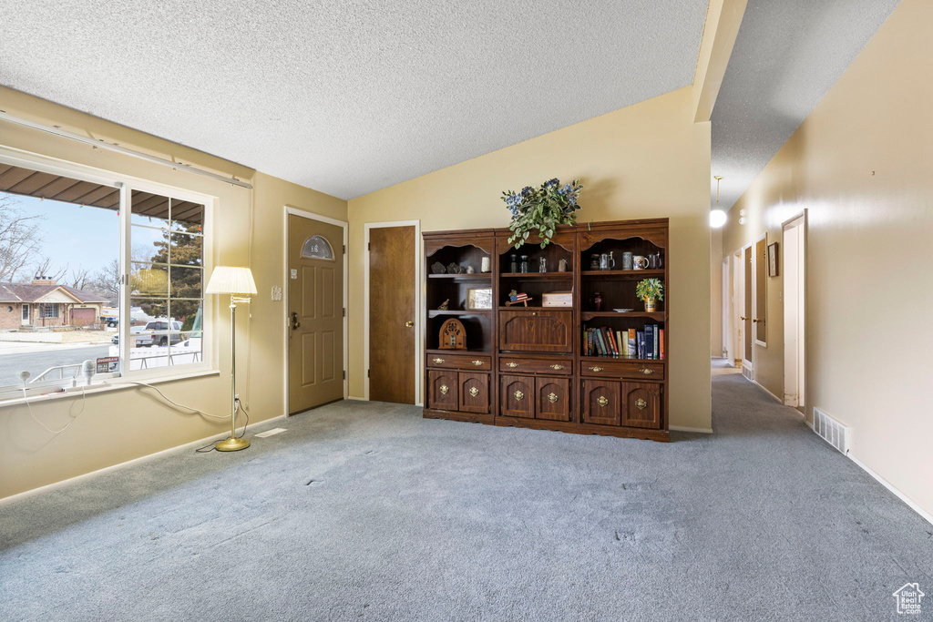 Carpeted spare room featuring visible vents, vaulted ceiling, and a textured ceiling