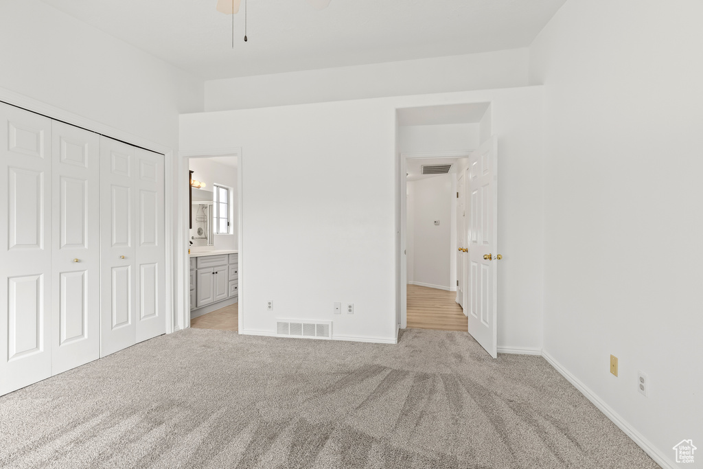 Unfurnished bedroom with a closet, connected bathroom, visible vents, and light colored carpet