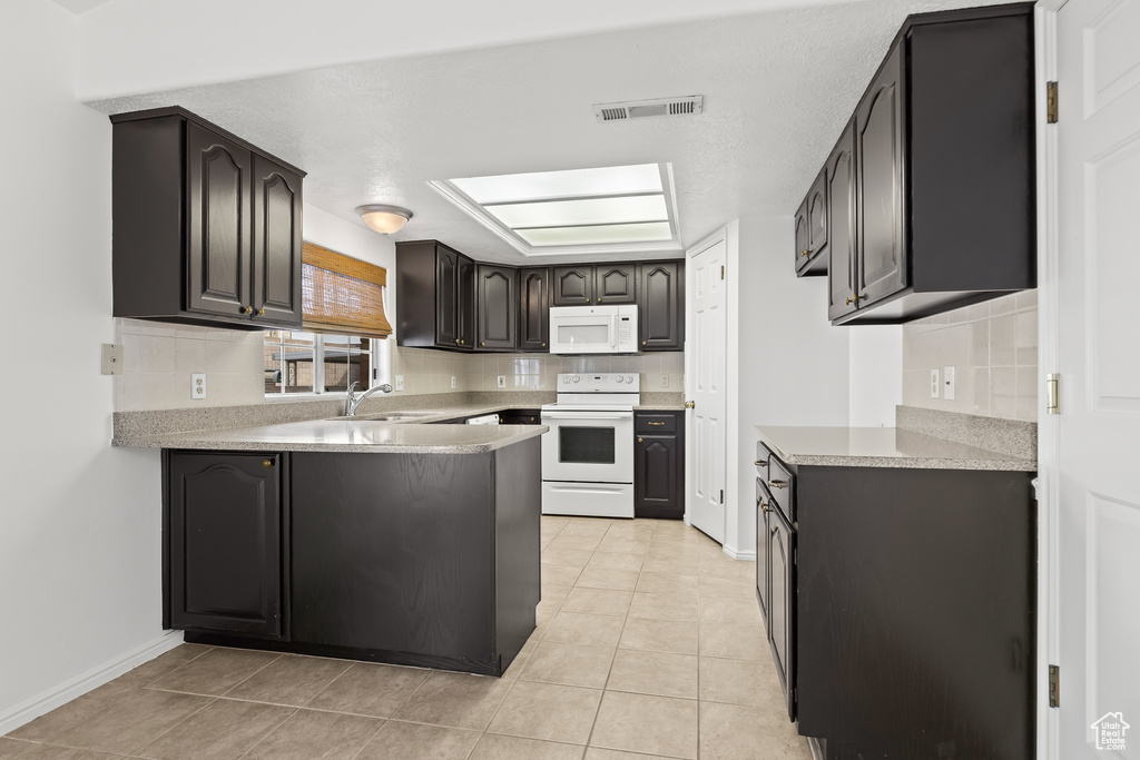 Kitchen with tasteful backsplash, light countertops, visible vents, white appliances, and a peninsula