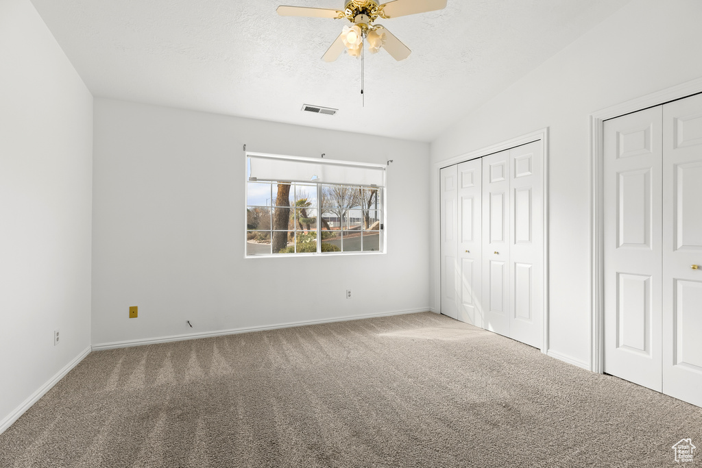 Unfurnished bedroom with baseboards, visible vents, a textured ceiling, carpet floors, and multiple closets