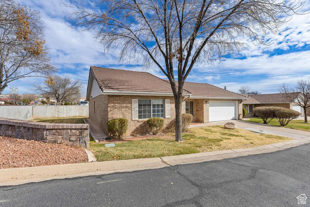 View of front of property featuring brick siding, concrete driveway, an attached garage, fence, and a front yard