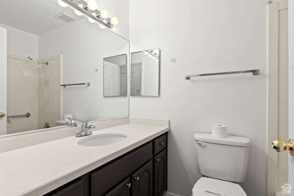 Bathroom featuring toilet, visible vents, a shower, and vanity