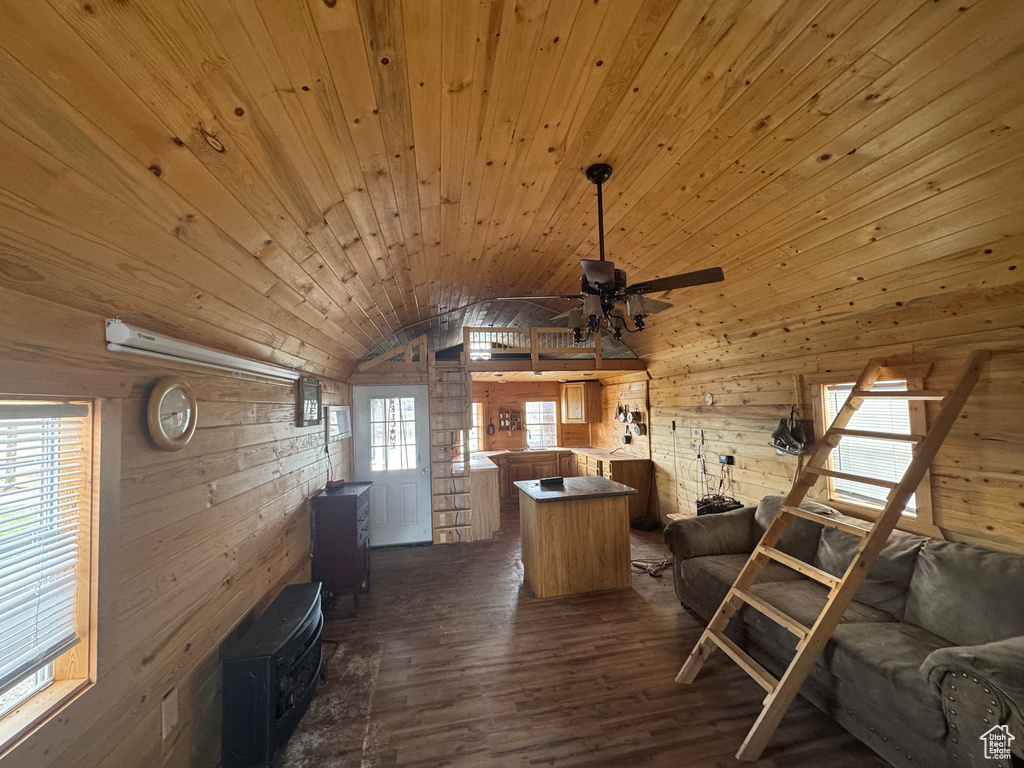 Living room with dark wood-style floors, wood walls, ceiling fan, vaulted ceiling, and a wood stove