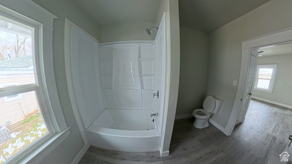 Full bath featuring toilet,  shower combination, wood finished floors, and baseboards