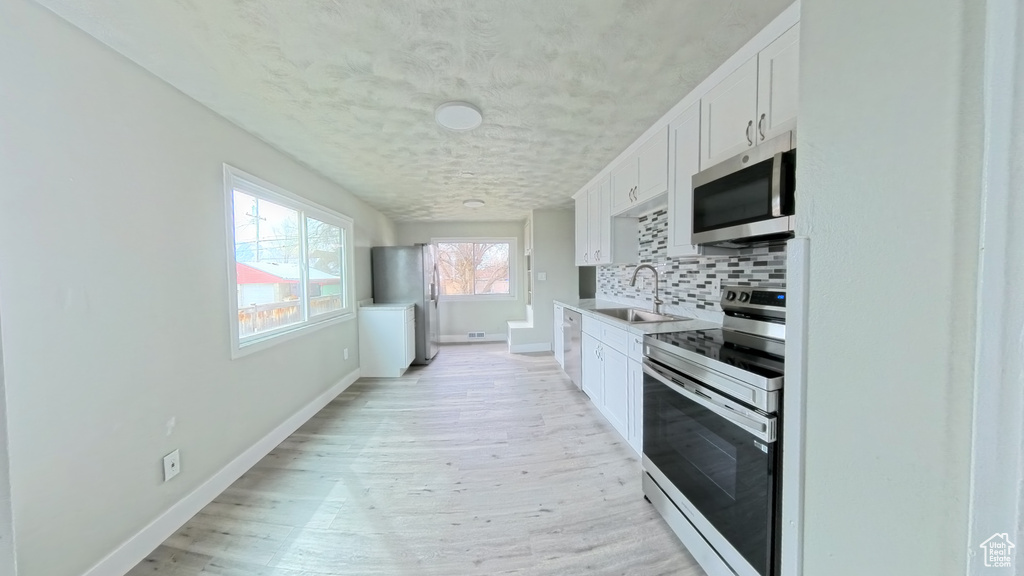 Kitchen featuring a sink, white cabinetry, stainless steel appliances, light wood-style floors, and decorative backsplash