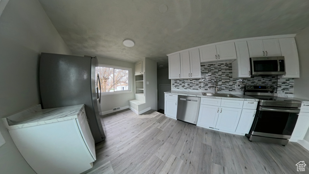 Kitchen featuring decorative backsplash, light countertops, stainless steel appliances, a sink, and light wood-style floors