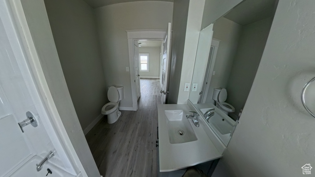Half bath with baseboards, wood finished floors, toilet, and vanity