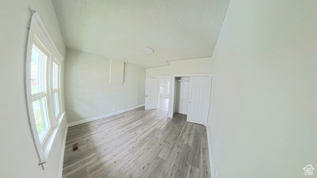 Empty room featuring light wood finished floors, baseboards, visible vents, and a textured ceiling