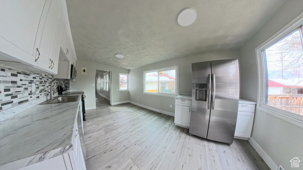 Kitchen featuring decorative backsplash, light wood finished floors, appliances with stainless steel finishes, white cabinetry, and a sink