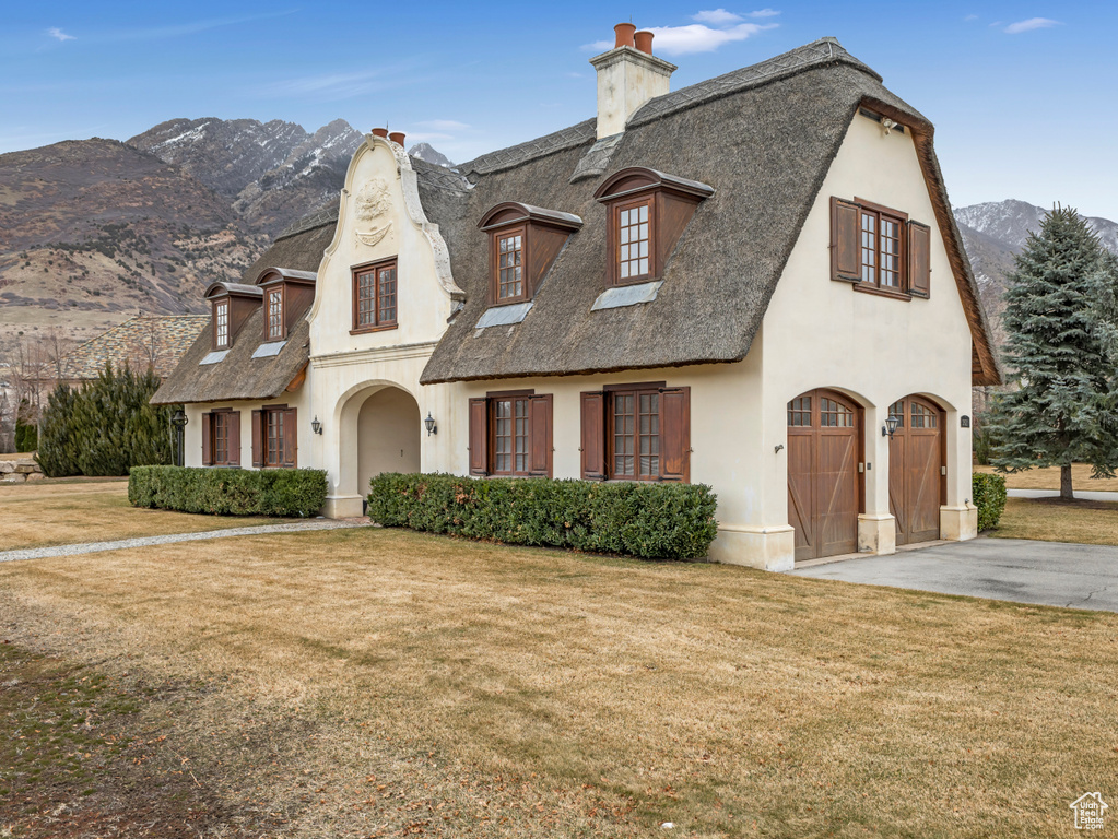 French provincial home featuring asphalt driveway, a chimney, a front yard, a mountain view, and stucco siding