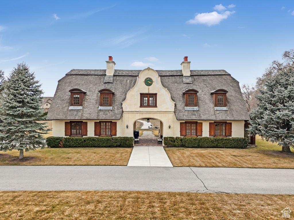 French country style house featuring a chimney, stucco siding, and a front lawn