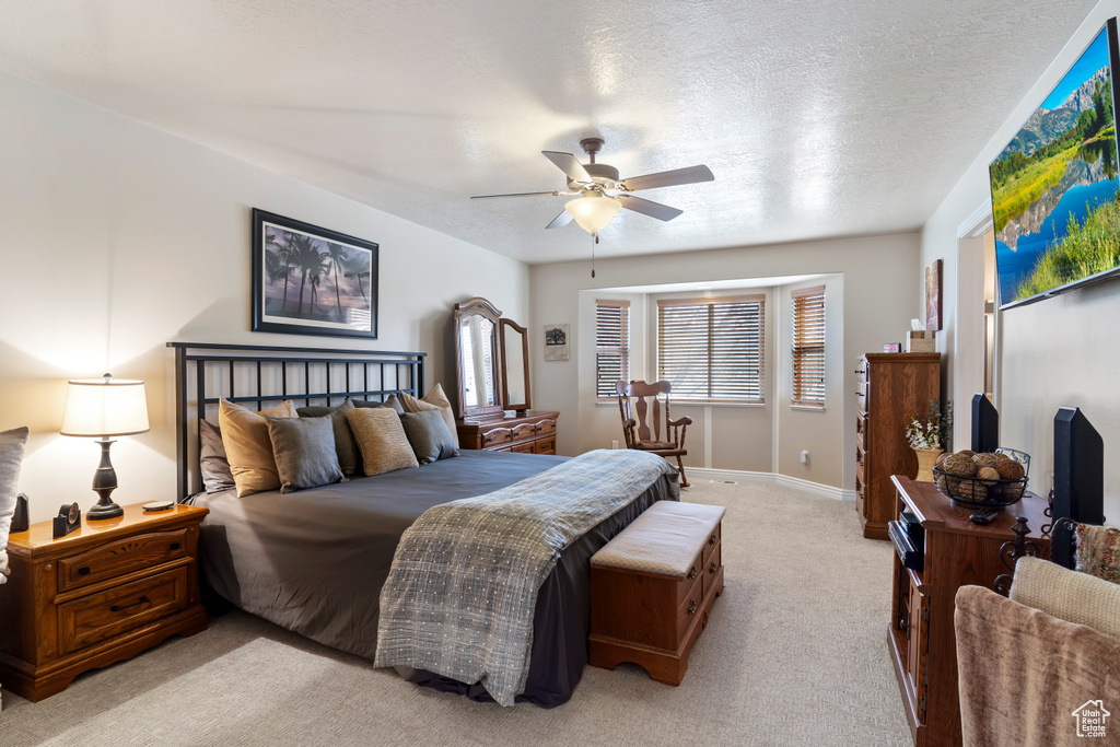 Bedroom with light carpet, a ceiling fan, baseboards, and a textured ceiling