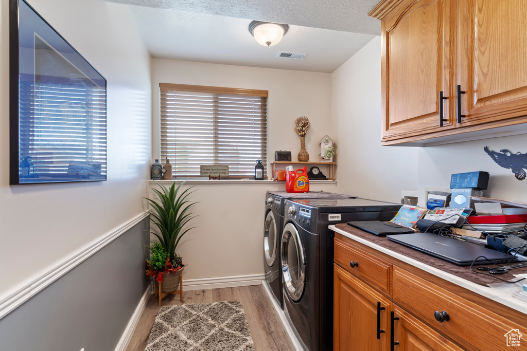 Laundry area with washer and clothes dryer, light wood finished floors, visible vents, cabinet space, and baseboards