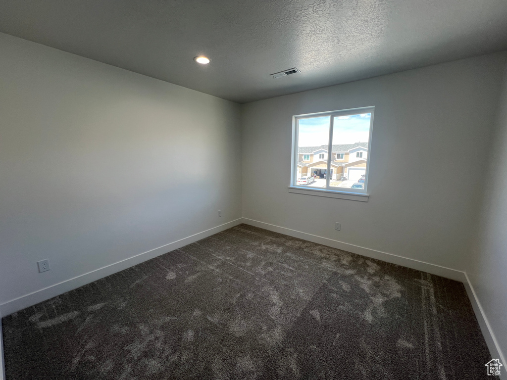 Empty room with baseboards, visible vents, and dark colored carpet