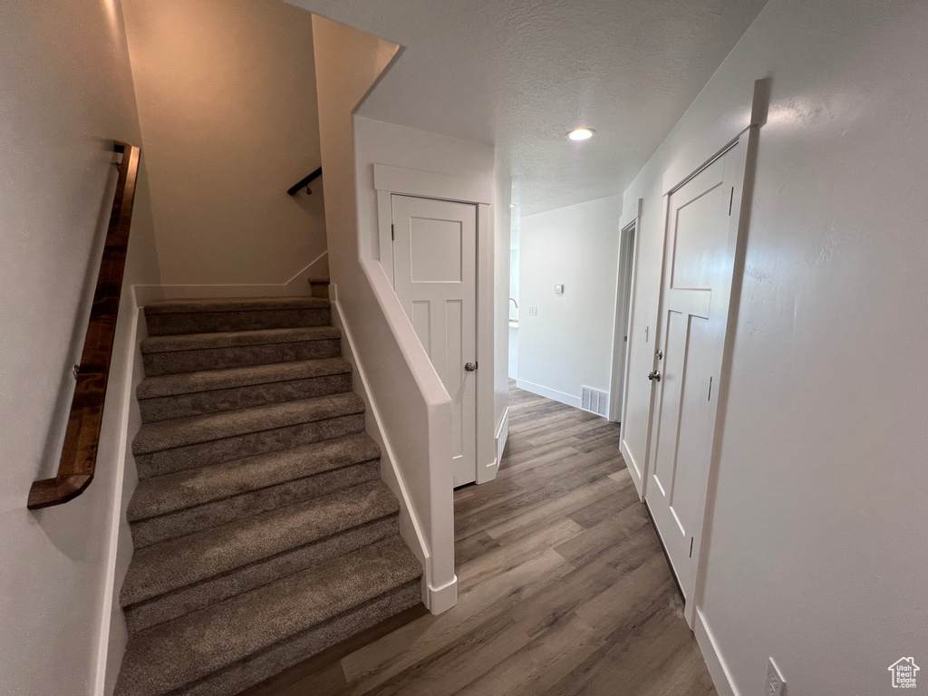 Stairs featuring a textured ceiling, recessed lighting, wood finished floors, visible vents, and baseboards